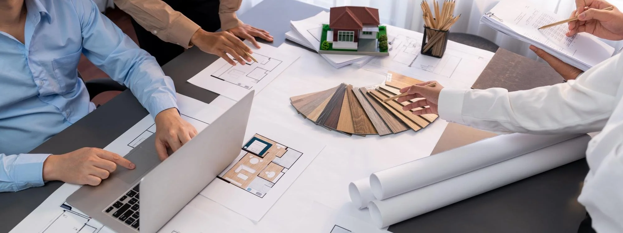 Architects and designers planning a house construction project with blueprints, color samples, and a miniature model of a house on a table.