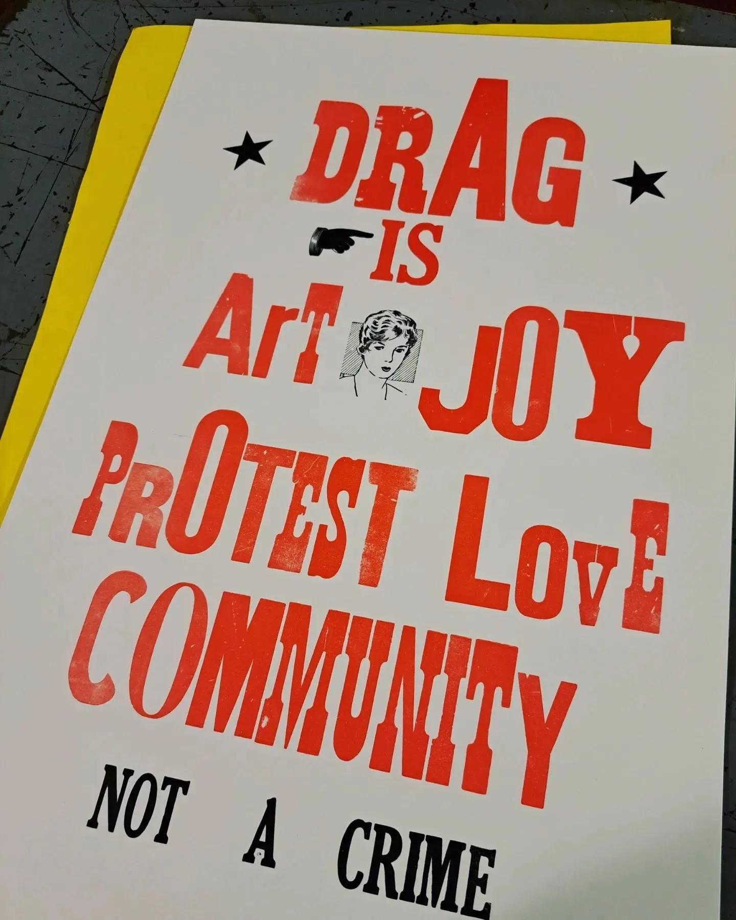 Close-up photograph of a red-and-black letterpress poster reading “Drag is art, joy, protest, love, community, not a crime.”