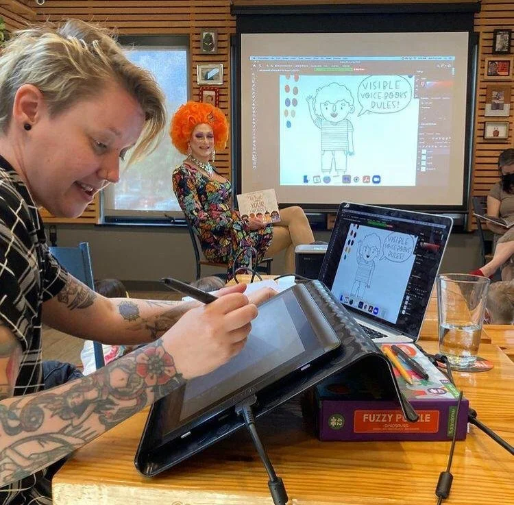 Photograph of Andy Passchier sitting with a drag performer in a casual indoor setting, both smiling and engaging in conversation, with a warm, candid documentary-style feel.