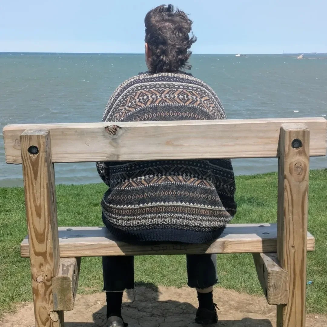 Portrait of Andy Passchier sitting on a wooden bench facing the sea.