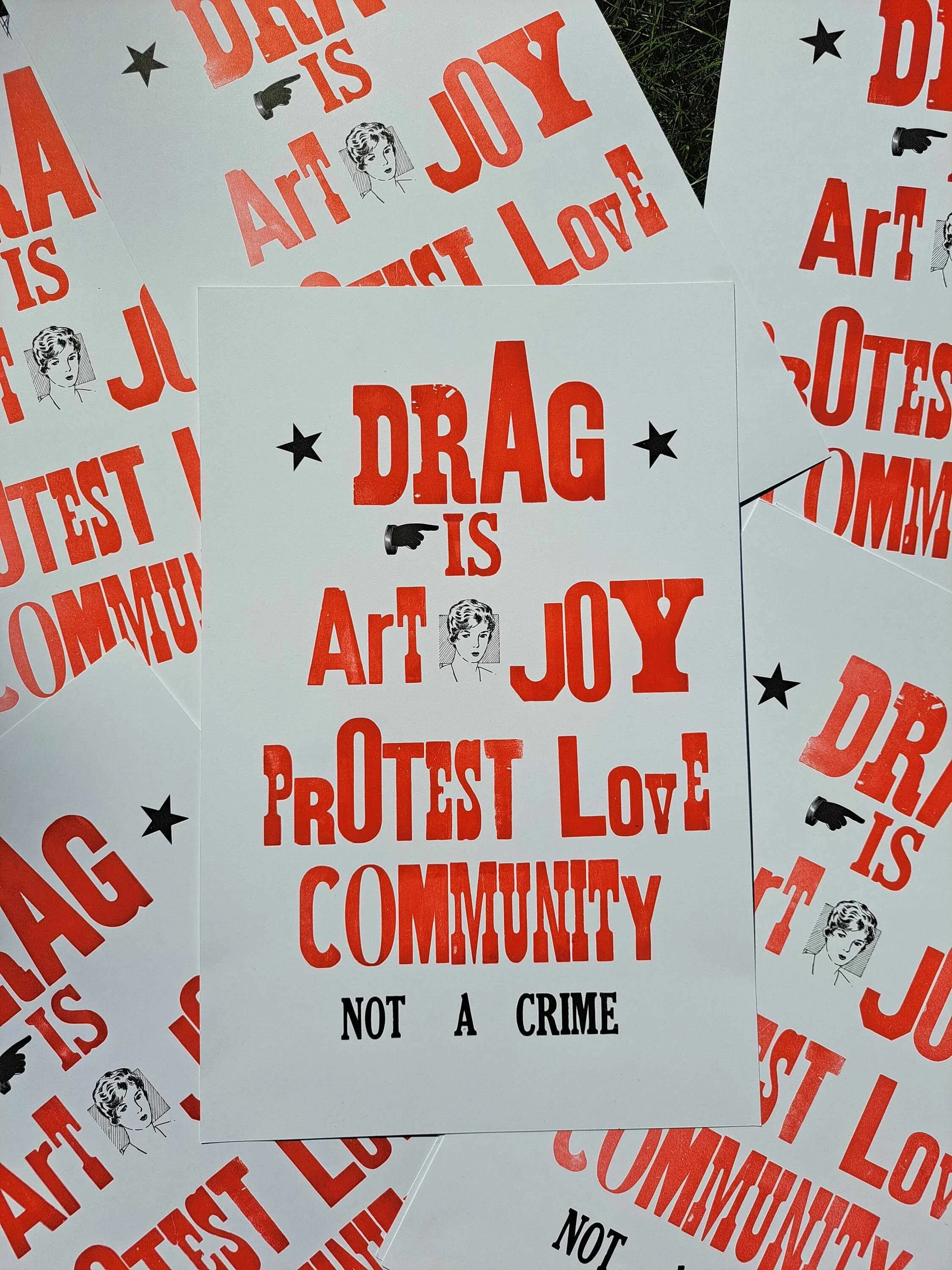 Close-up photograph of overlapping red-and-black “Drag Is Art” letterpress posters scattered across a white surface.
