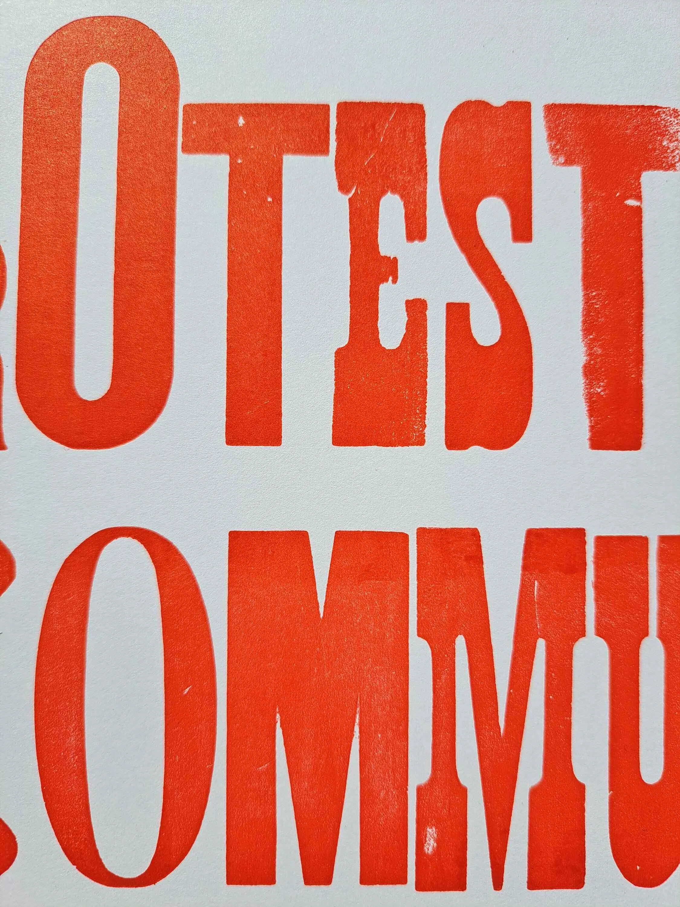 Close-up photograph of oversized red letterpress text reading “protest” and “community” on a white poster background.