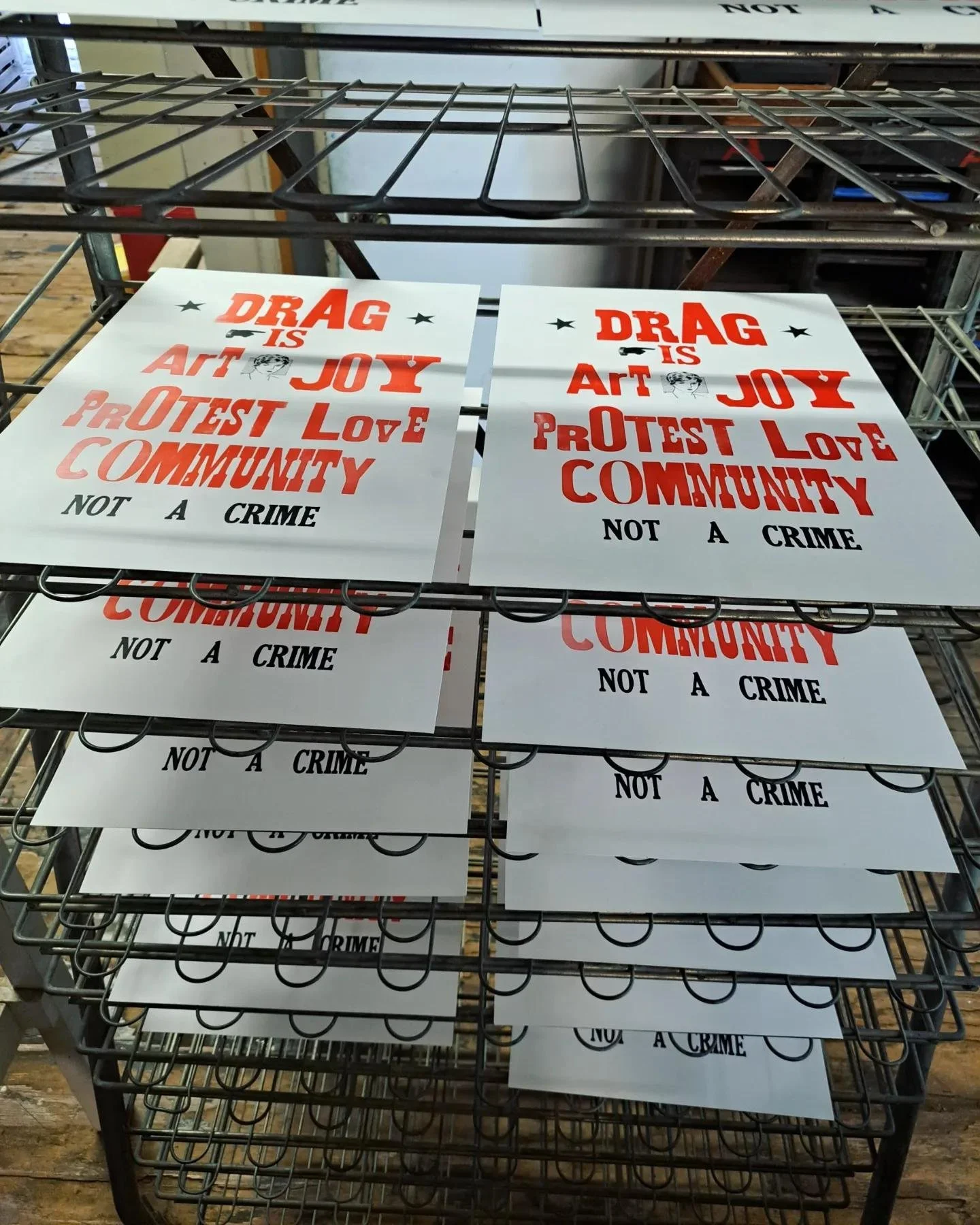 Process photo of freshly printed “Drag Is Art” letterpress posters drying on a metal print rack.