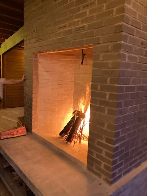 A brick fireplace with a fire burning inside, located in a room with wooden walls and ceiling.