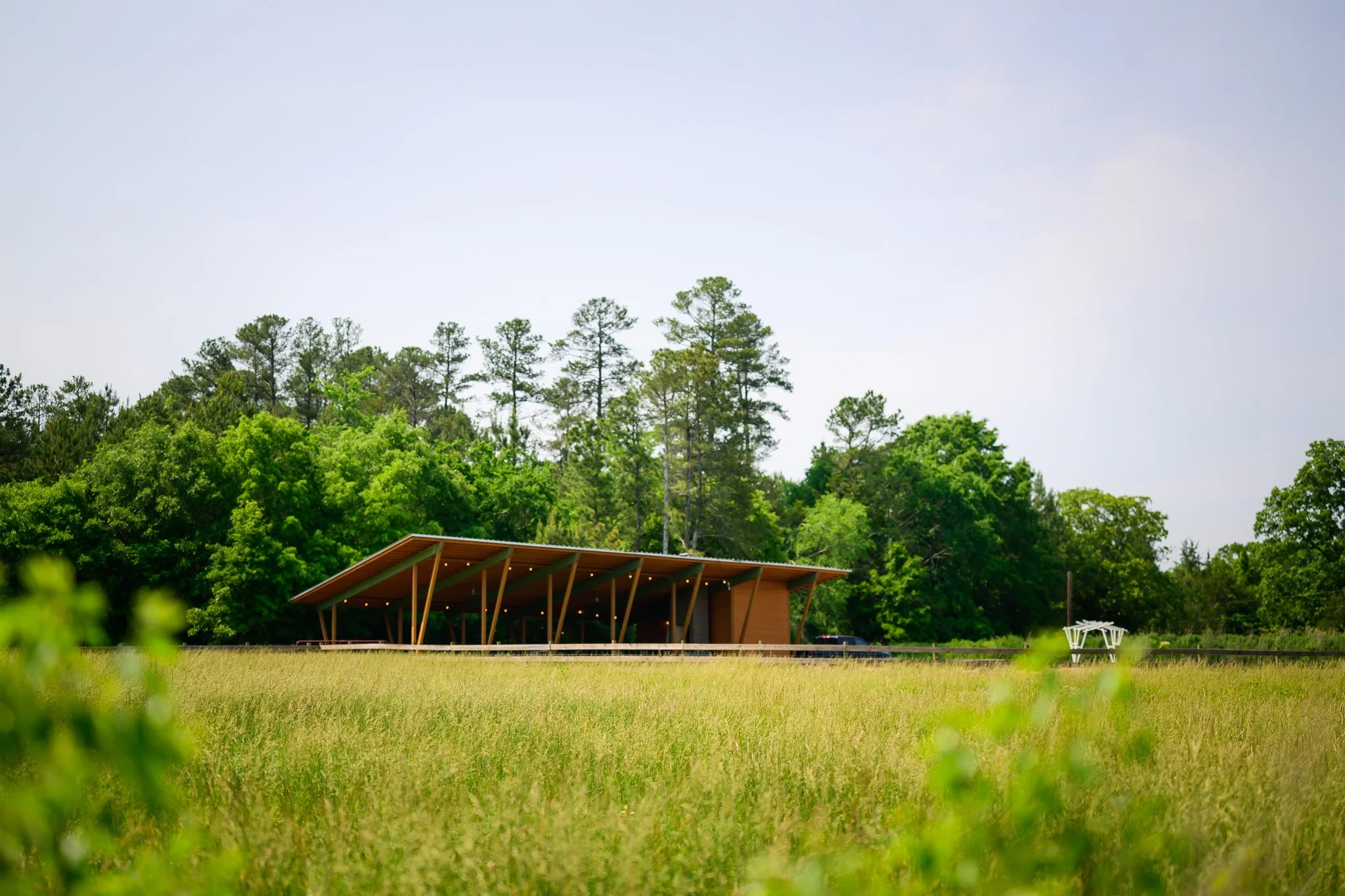 Modern building with a wooden roof in front of a lush green forest under a cloudy sky.