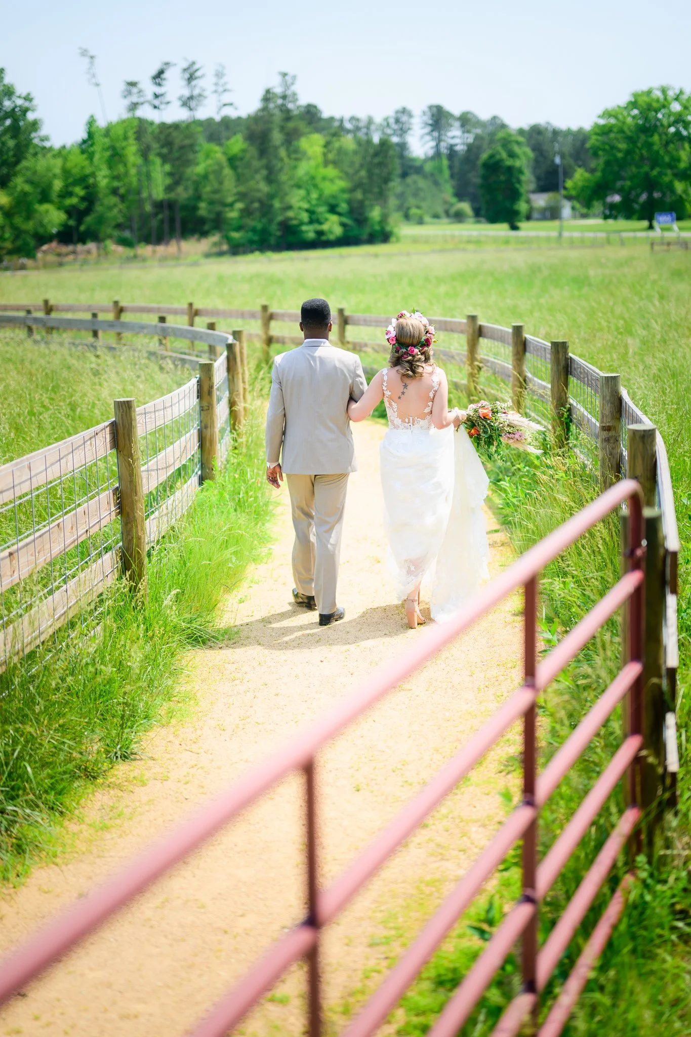 A bride and groom holding hands and walking down a wooded path on their wedding day, with lush green trees in the background.