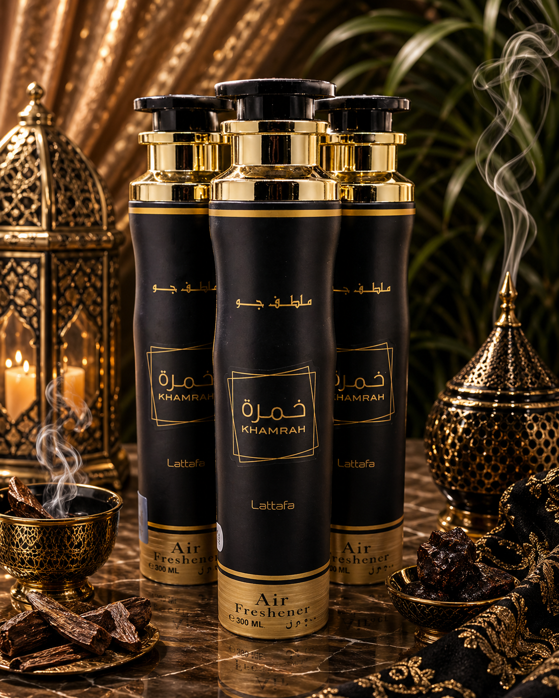 Three cans of black and gold air freshener labeled 'Khamrah' arranged on a marble surface with ornate gold and black decorative items and leather strips around them.