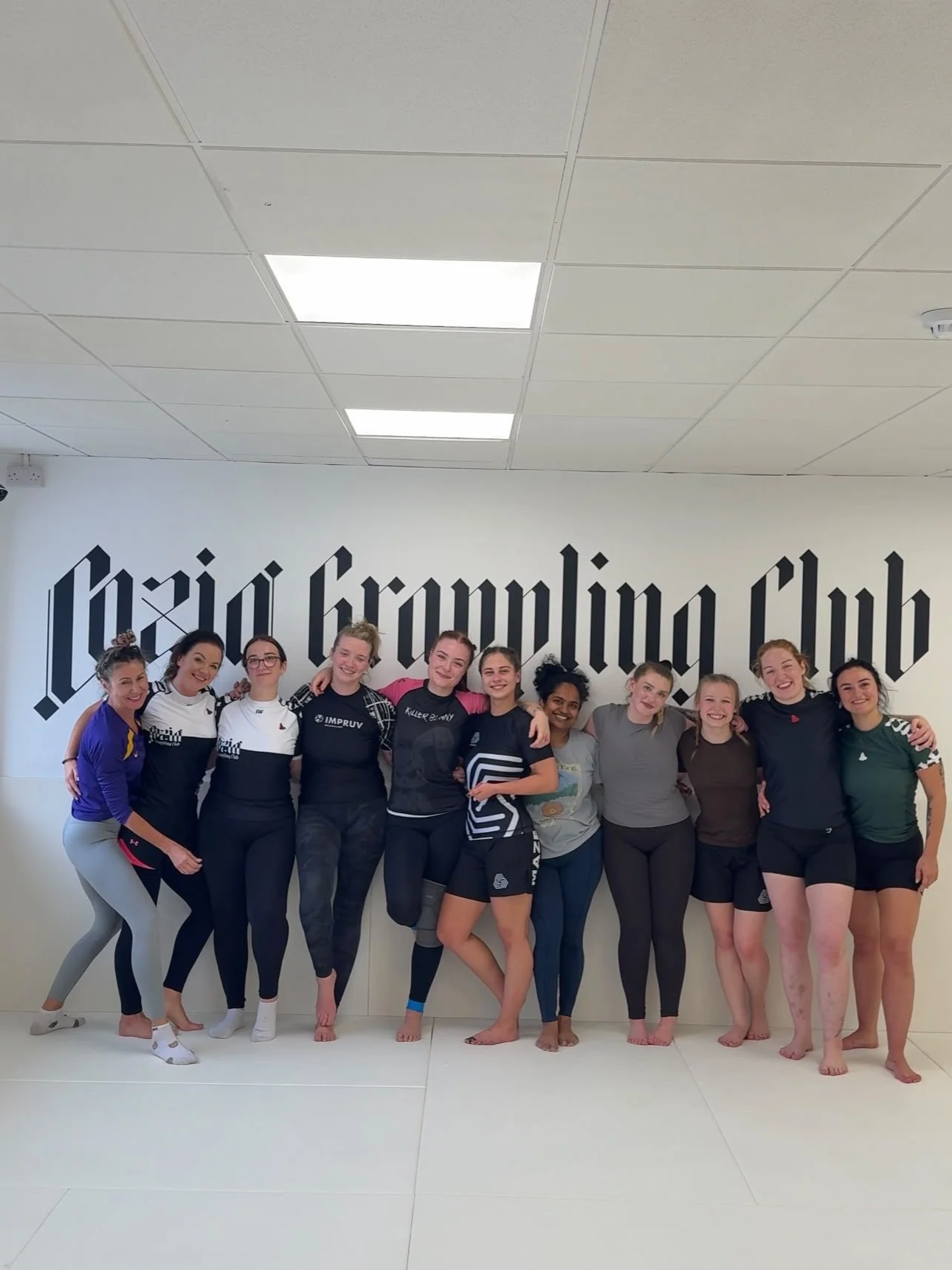 Group of women standing together in a gym, smiling and posing for a photo.