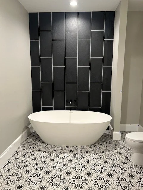 Modern bathroom with a freestanding oval bathtub, black tiled accent wall, and patterned tile floor.