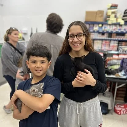 A boy and a girl holding kittens inside a pet store.