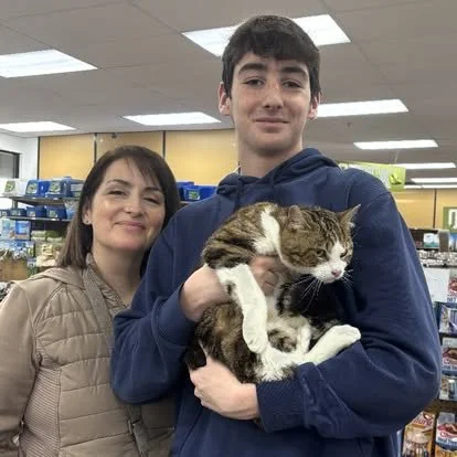 A young man holding a tabby cat in a pet store with a woman standing next to him.