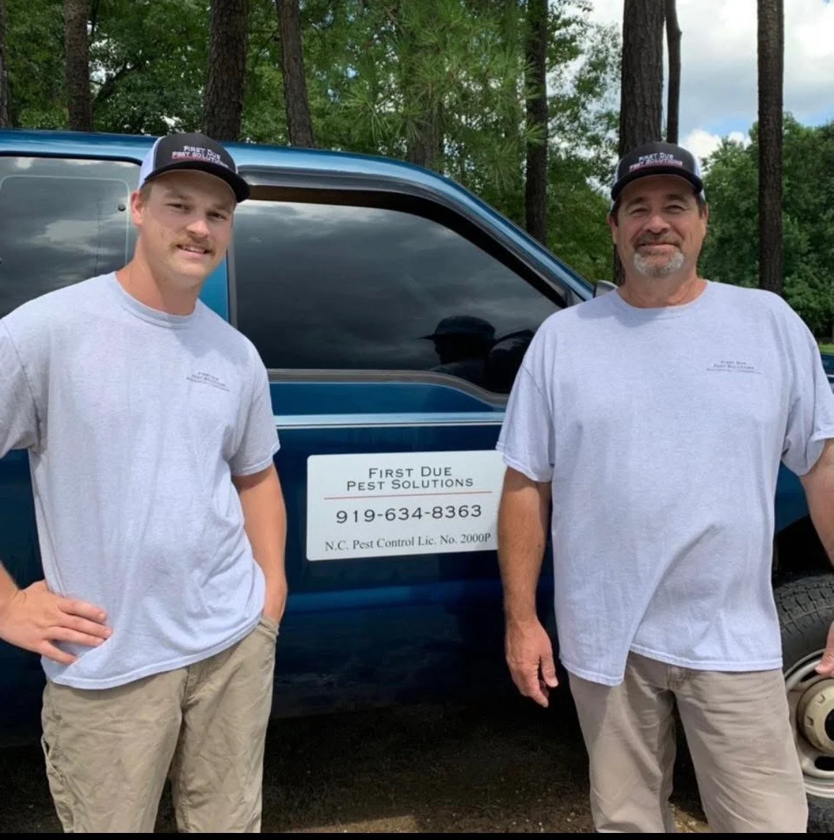 Two men standing in front of a truck with a sign that reads 'First Due Pest Solutions' and a phone number, in a wooded outdoor setting.