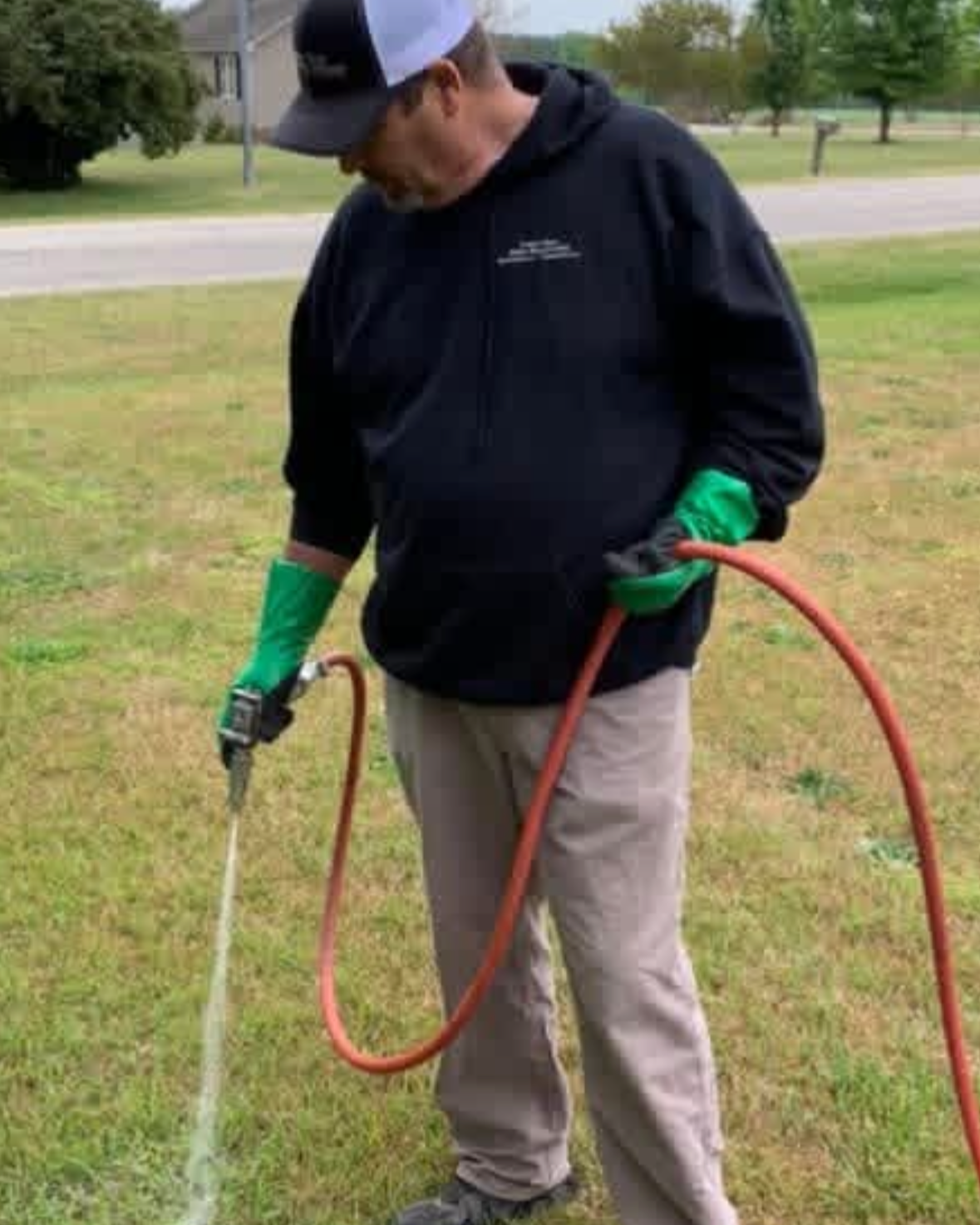 A pest control technician is treating a yard for moquitoes with a spray nozzle.