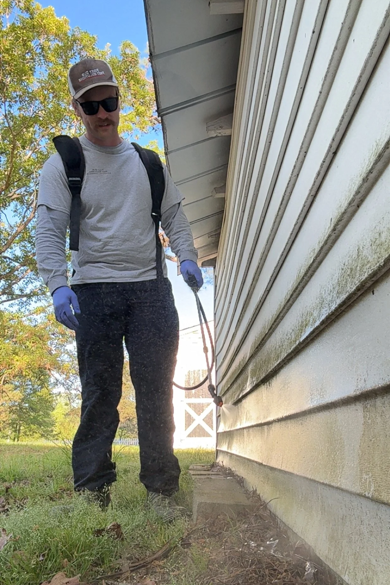 A pest control technician is treating the base of a home for household pest prevention.