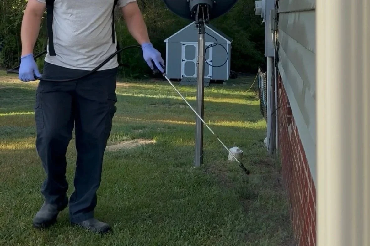 Exterminator spraying the outside of a home foundation to prevent termites and other pests from entering.