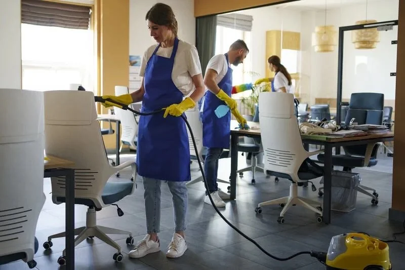 Office cleaning team with blue aprons and gloves cleaning furniture and floors.