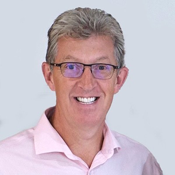 A smiling man with gray hair, glasses, and a pink collared shirt.