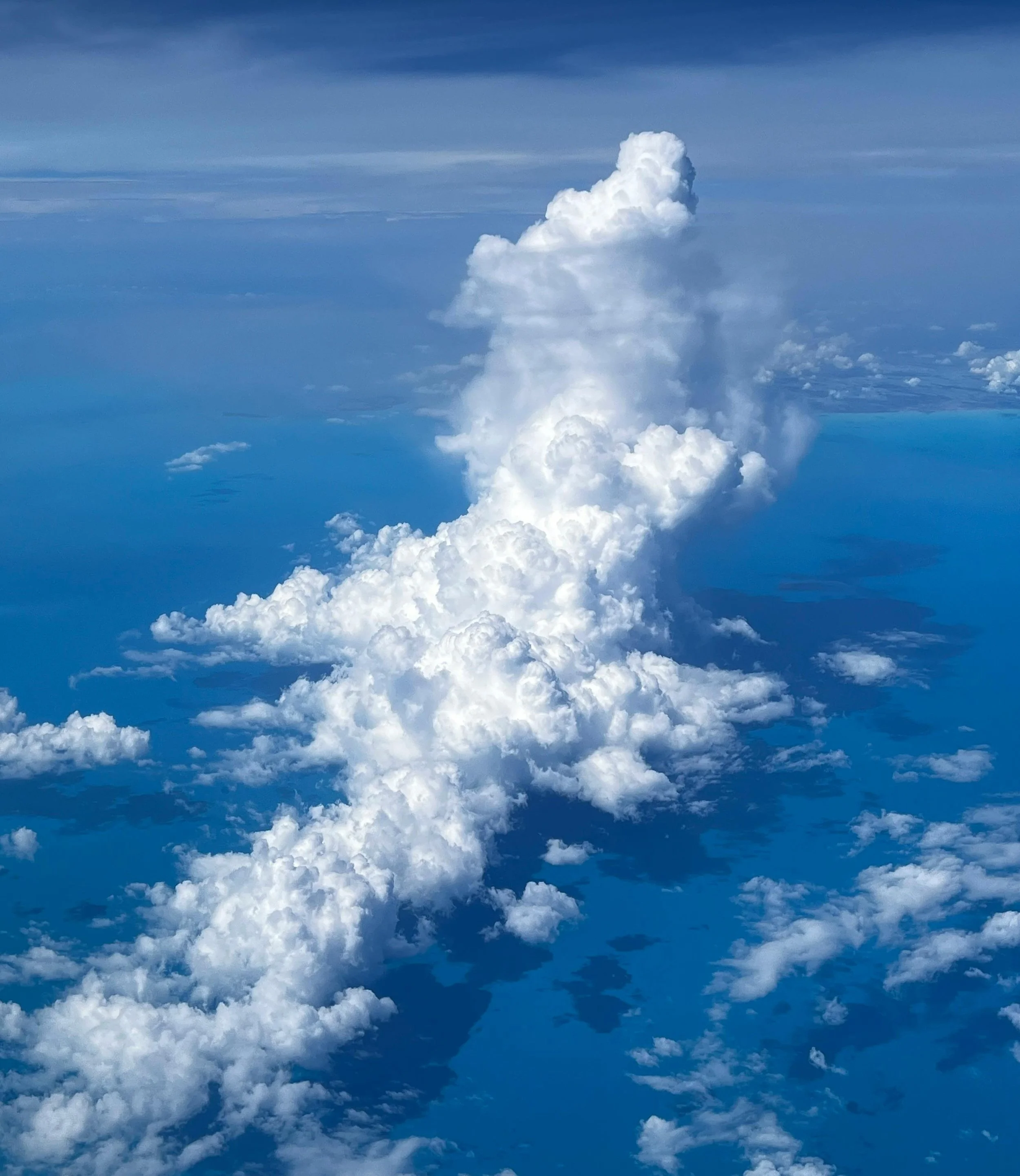 A large, towering cumulus cloud formation extending through the sky over the ocean.