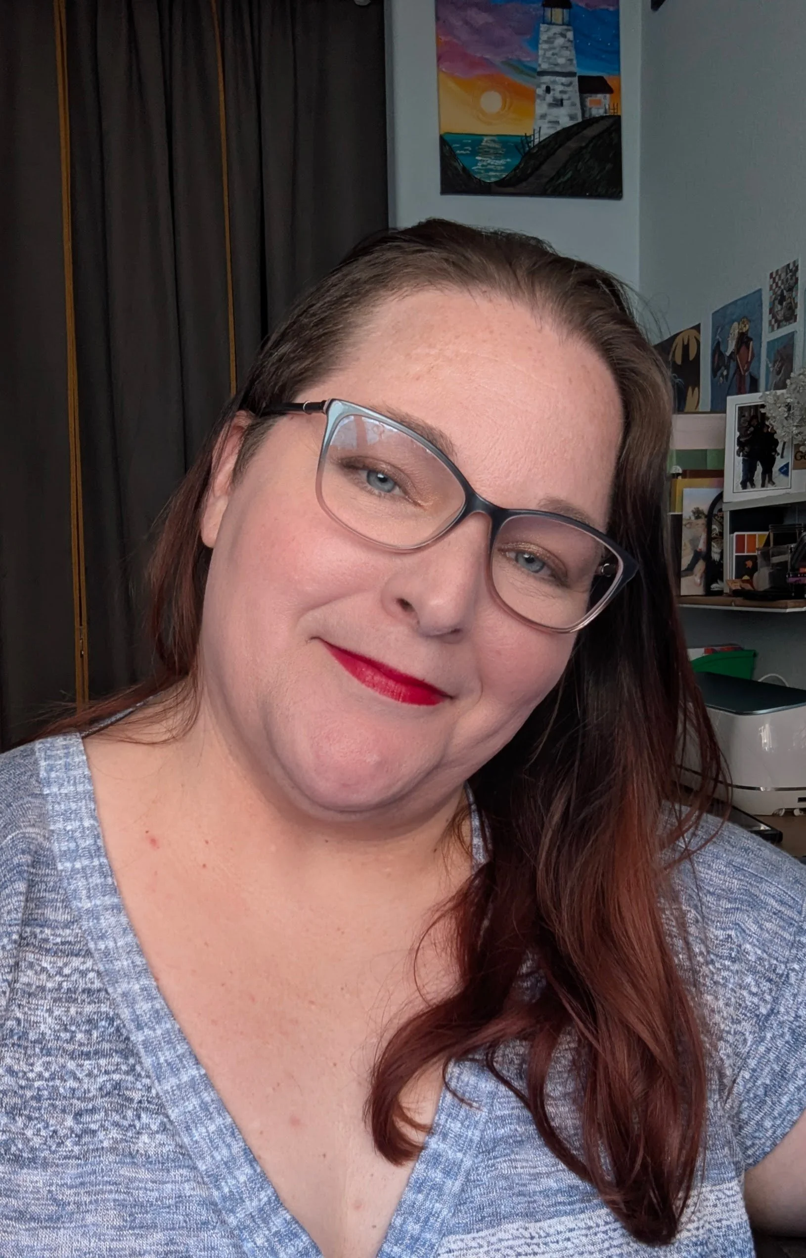 A woman with glasses and red hair smiling for a selfie indoors.