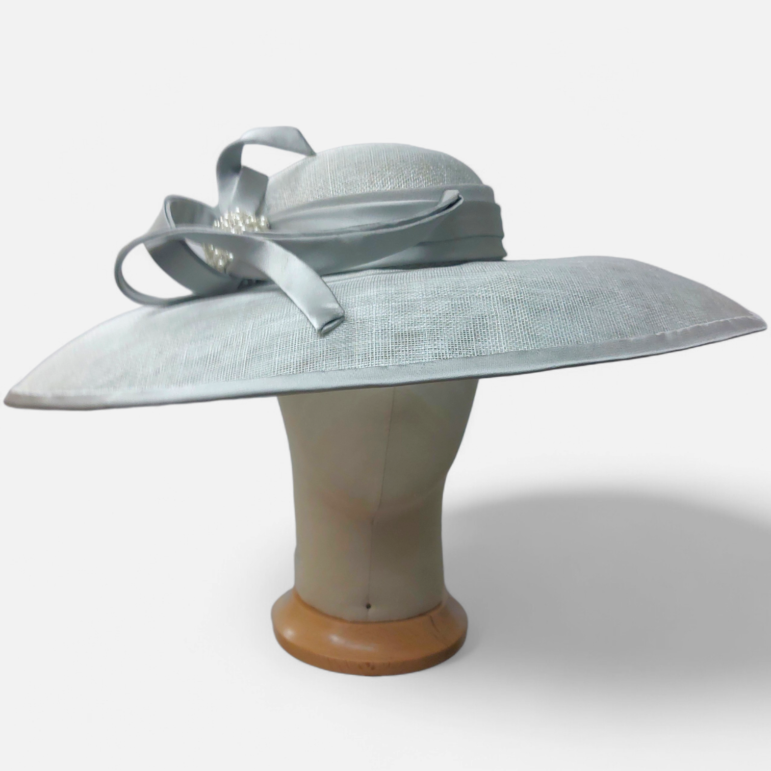 A large mint green wide-brimmed hat from John Paul Millinery, with a decorative fabric bow, displayed on a mannequin head form.