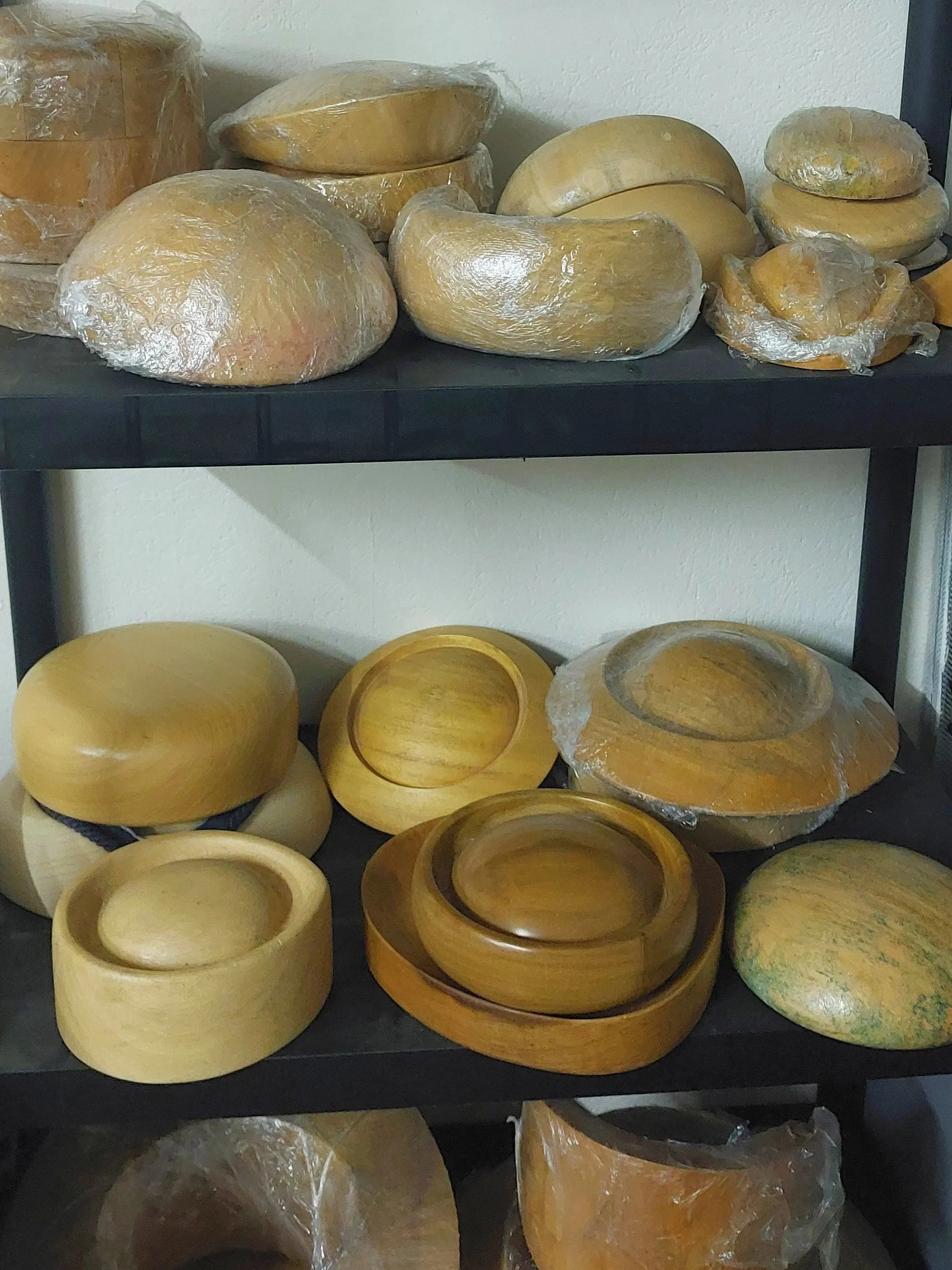 Various wooden hat blocks, some new some vintage, covered in plastic wrap displayed on shelves at John Paul Millinery studio in Derry.