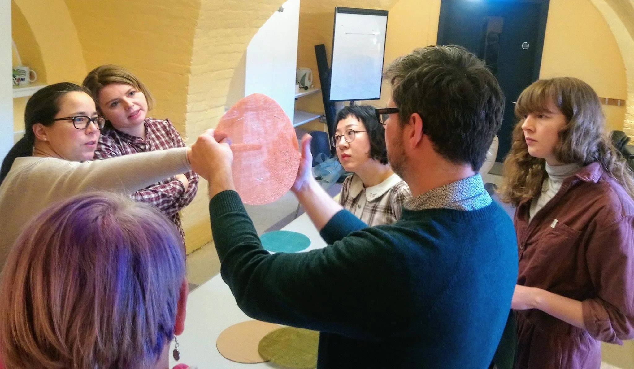 A group of students gathered around John Paul during a demonstration at his millinery workshop