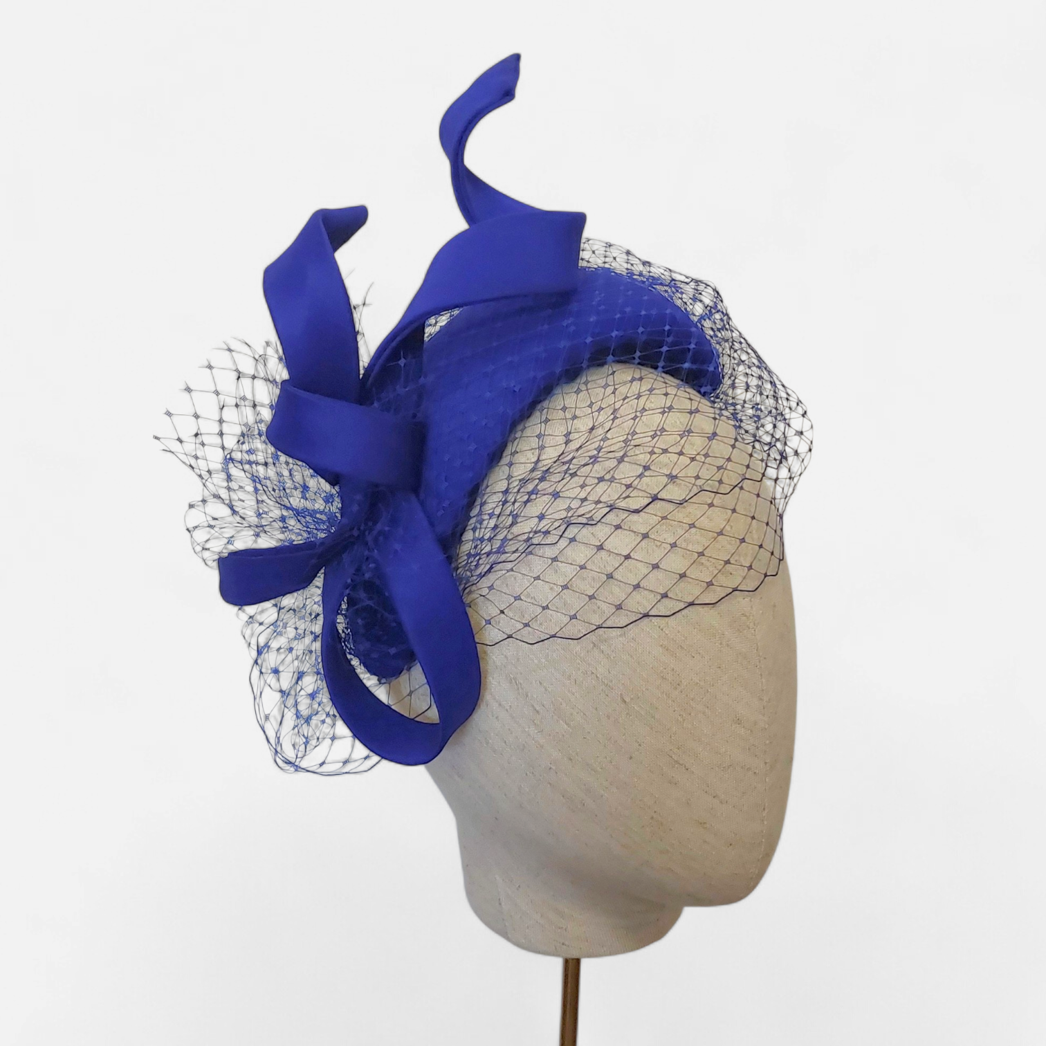 Blue John Paul Millinery fascinator with swirl and mesh veil displayed on a mannequin head.
