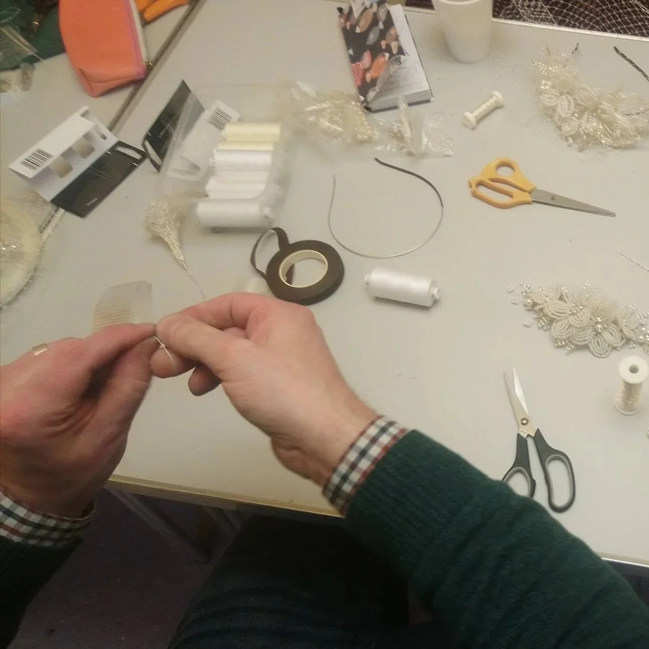 John Paul's hands making French Beaded Flowers, his work table has scissors, spools of wire thread, and beads on it.