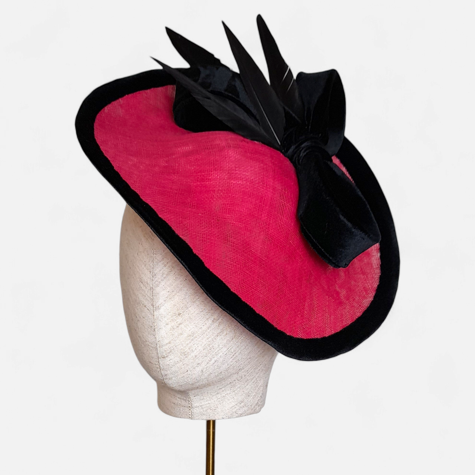 Cerise and black percher hat from John Paul Millinery, with a large black bow and black feather accents displayed on a mannequin head.