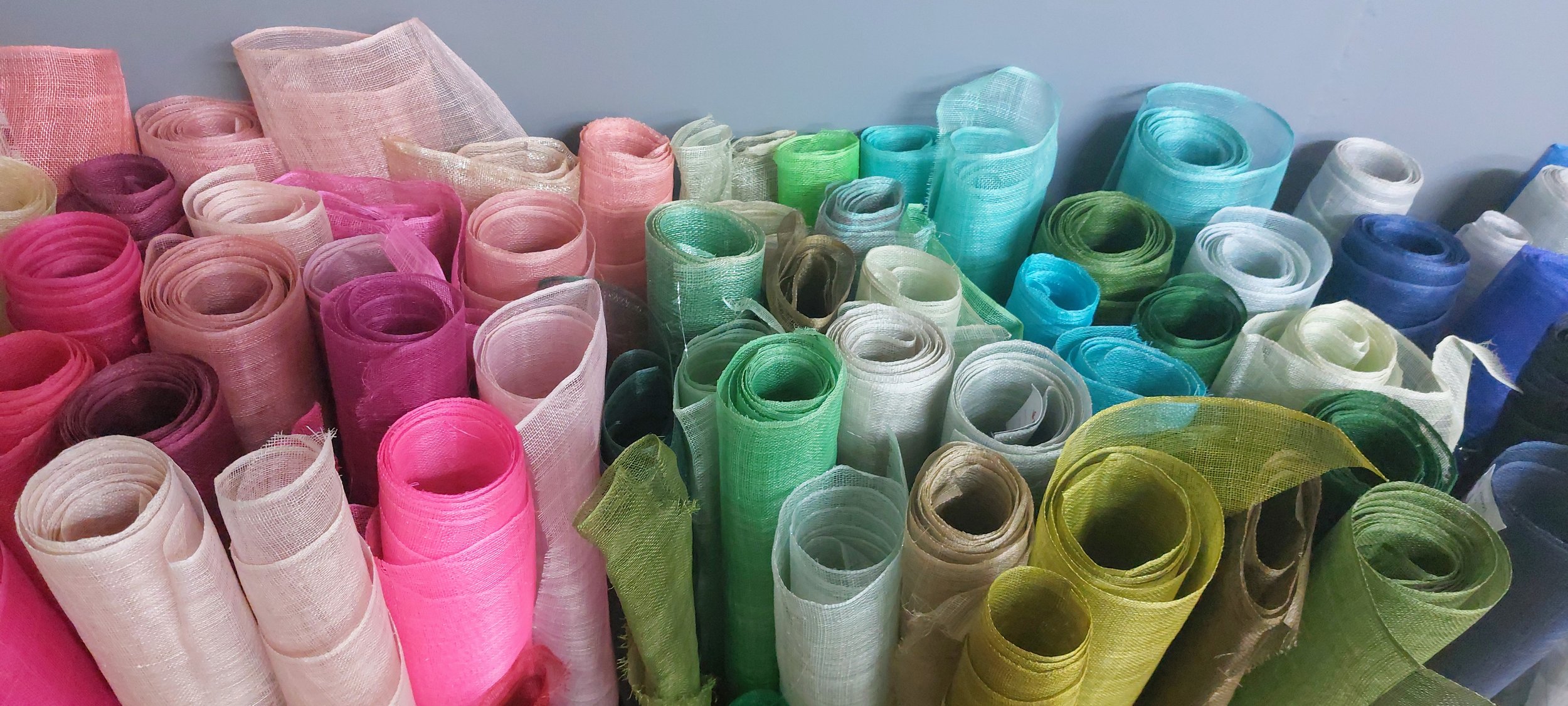 A collection of colorful sinamay fabric rolls, including pink, white, green, blue, and yellow, in John Paul Millinerys studio
