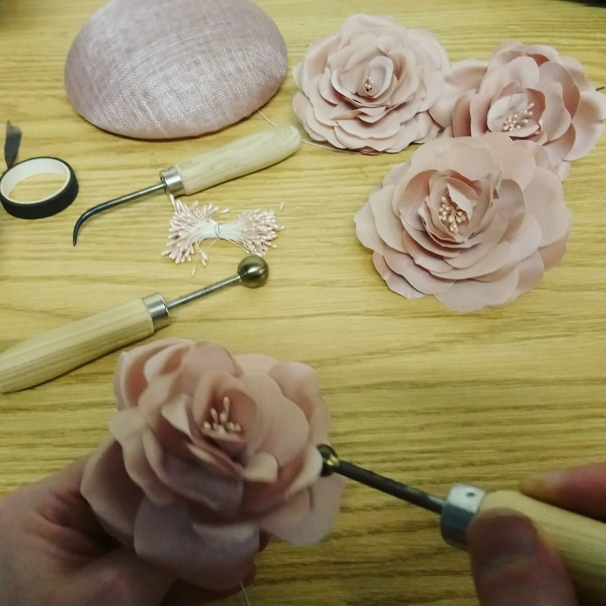 Close-up of John Paul's hand holding a flower making tool as he creates a handmade silk flower for one of his millinery designs