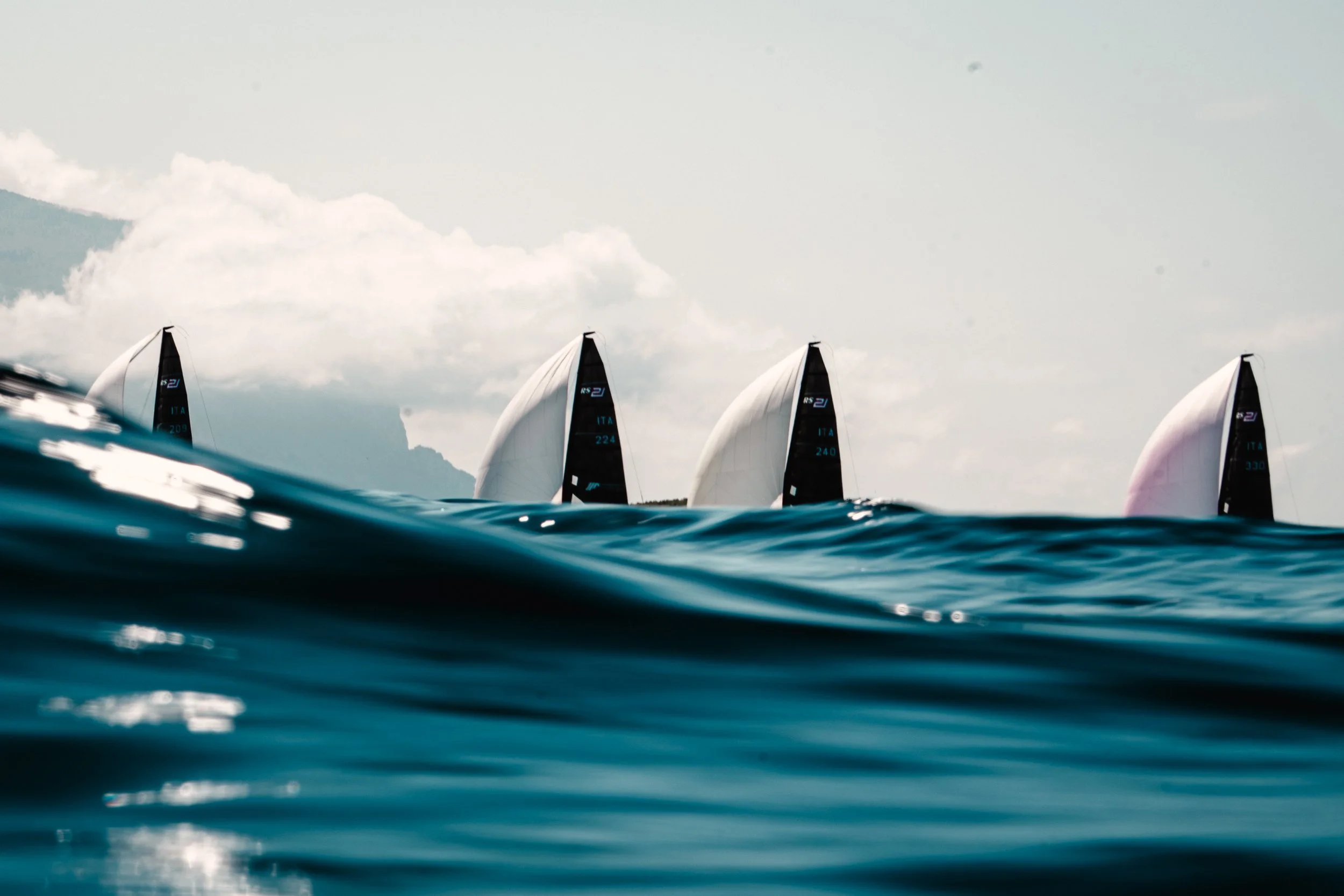 Vedute di barche a vela che navigano sull'acqua con le vele spiegate, sotto un cielo nuvoloso