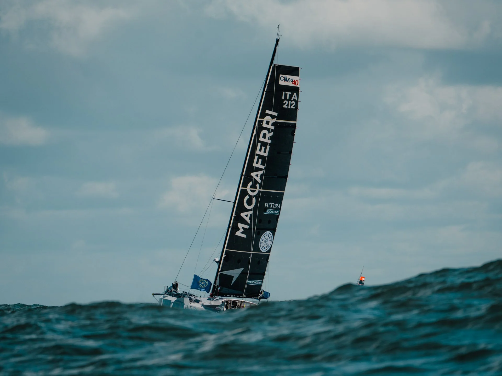 Una barca a vela con vele nere e grafiche, naviga tra le onde del mare durante una giornata nuvolosa.