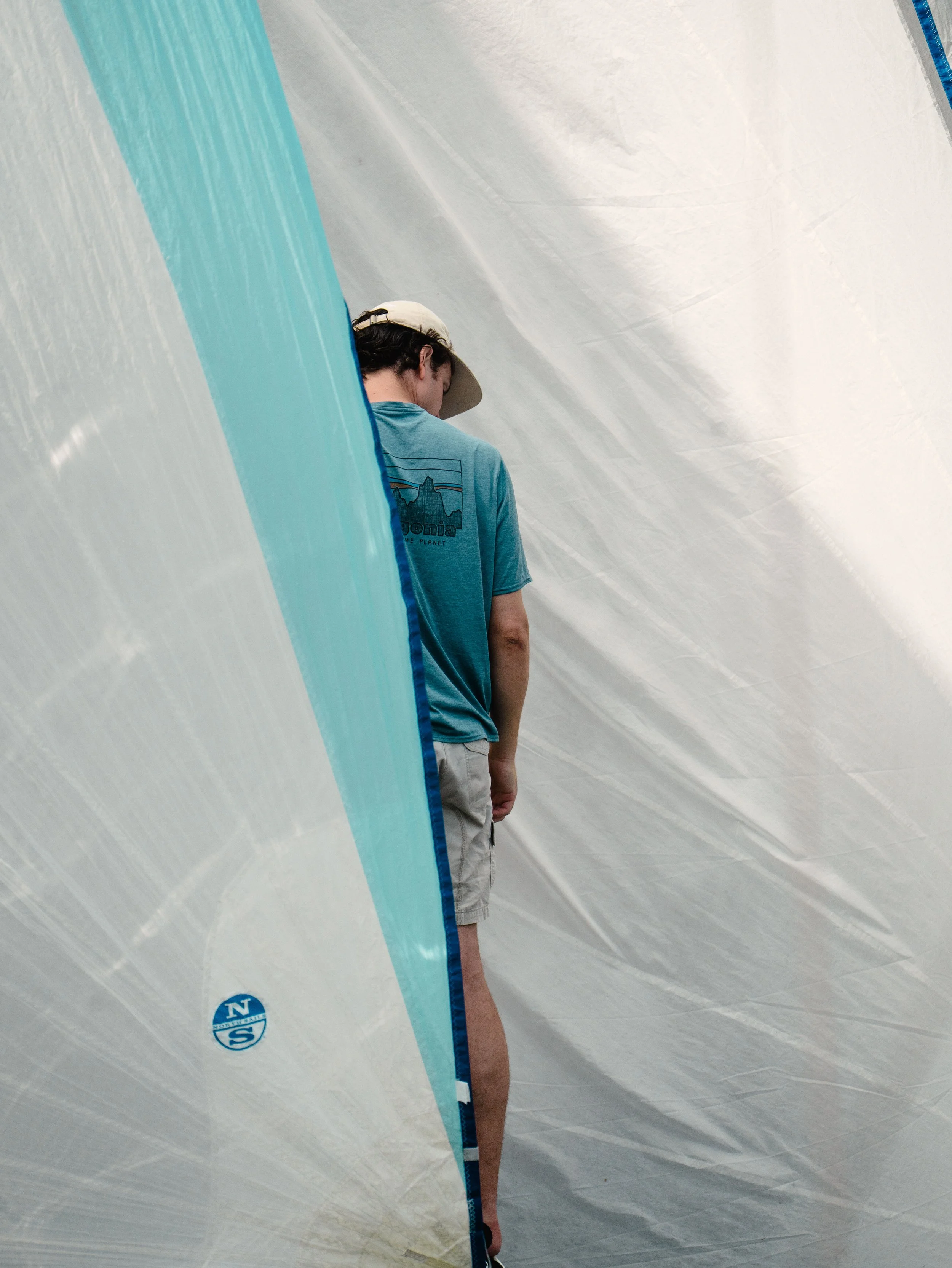 Giovane con cappellino e maglietta blu che si gira mentre si trova dietro una tenda da campeggio trasparente