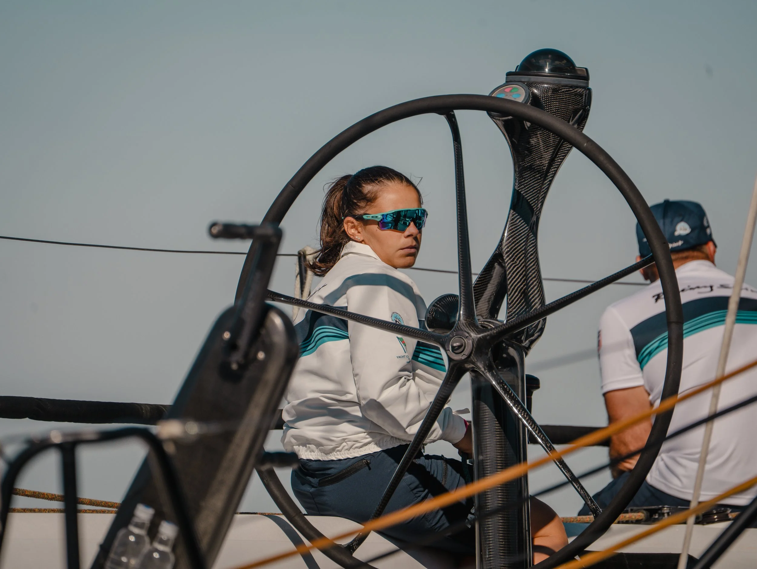 Donna seduta in un velivolo con casco e occhiali da sole sportivi, circondata da strutture di carbonio, mentre altri membri dell'equipaggio sono visibili sullo sfondo.