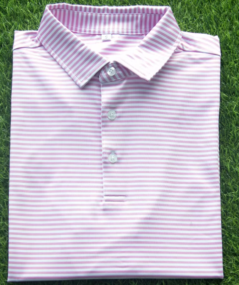 Folded pink and white striped polo shirt on grass.