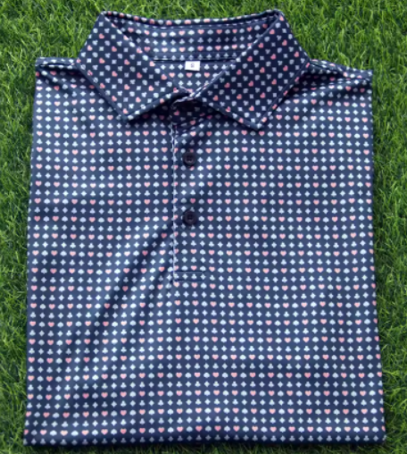 A folded navy blue polo shirt with small pink and white polka dots, lying on green grass.