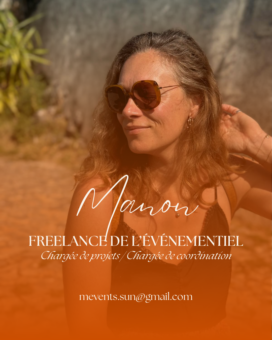 Une femme souriante portant des lunettes de soleil, avec des cheveux bouclés, dans un environnement en plein air avec des rochers et des plantes, utilisant une carte de visite ou une affiche