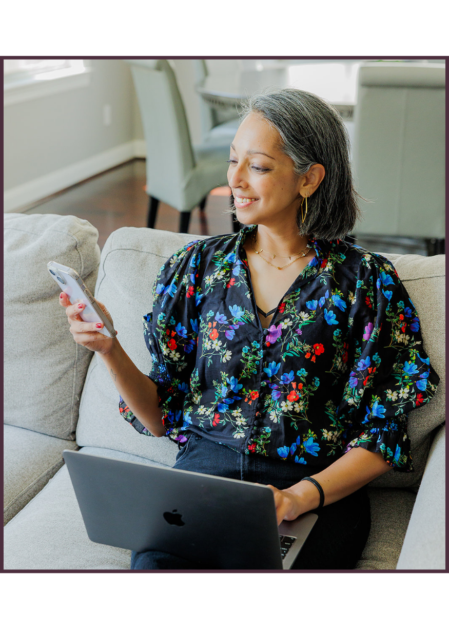 Aditi Pemmaraju, Houston physician relocation realtor, sitting on a sofa using her phone with a laptop nearby and smiling