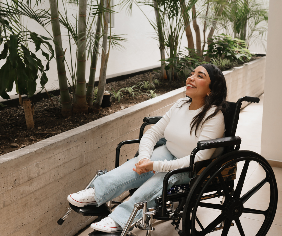 Woman in a wheelchair smiling while sitting next to a planter with green plants.