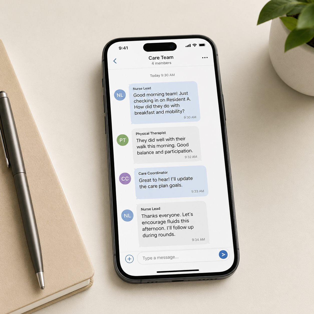 Smartphone displaying a group chat named Care Team with four members, including messages about patient care and updates, placed on a beige notebook with a silver pen on a white desk with a plant in the background.