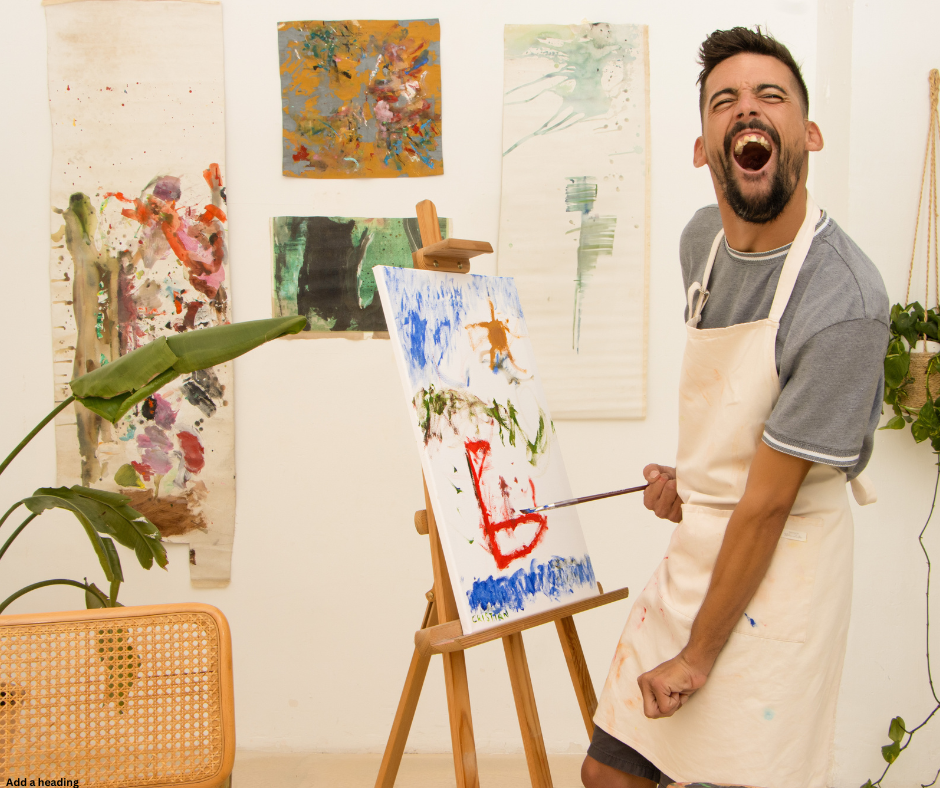 A man wearing an apron stands in an art studio, happily painting a canvas with a blue sky, a brown horse, and a red heart. The studio is decorated with colorful abstract paintings on the walls, and there is a large green plant to the left.