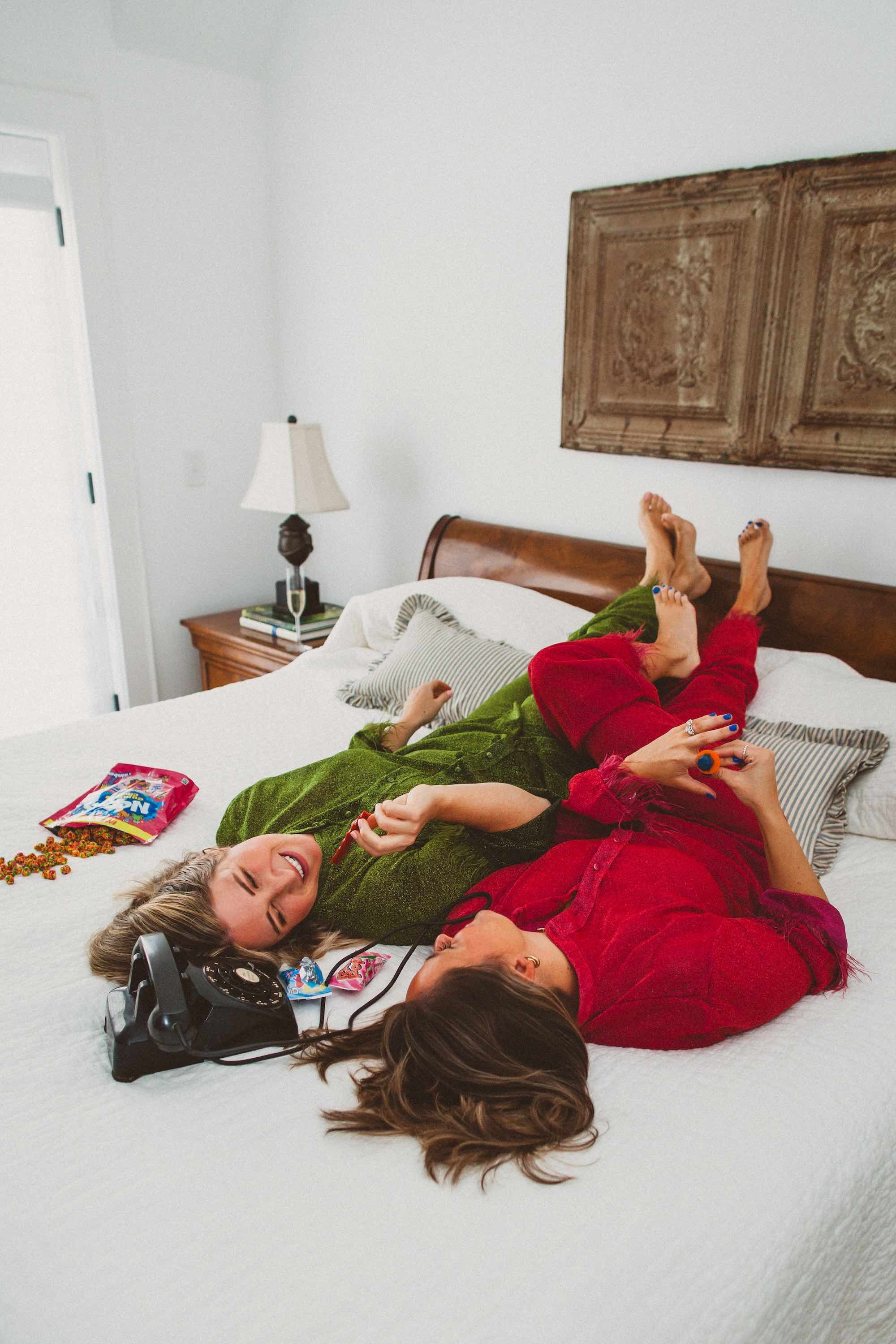 Two women lying on a bed, smiling and playing with candy, with old-fashioned telephone nearby.