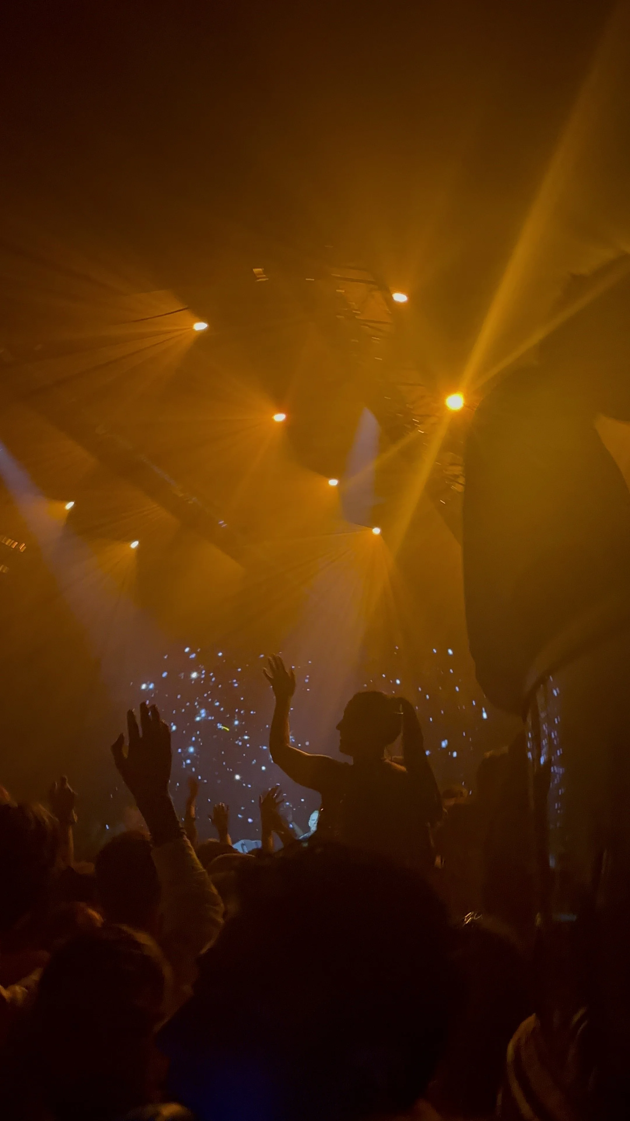 People dancing at a concert with orange stage lighting and star-like light effects.