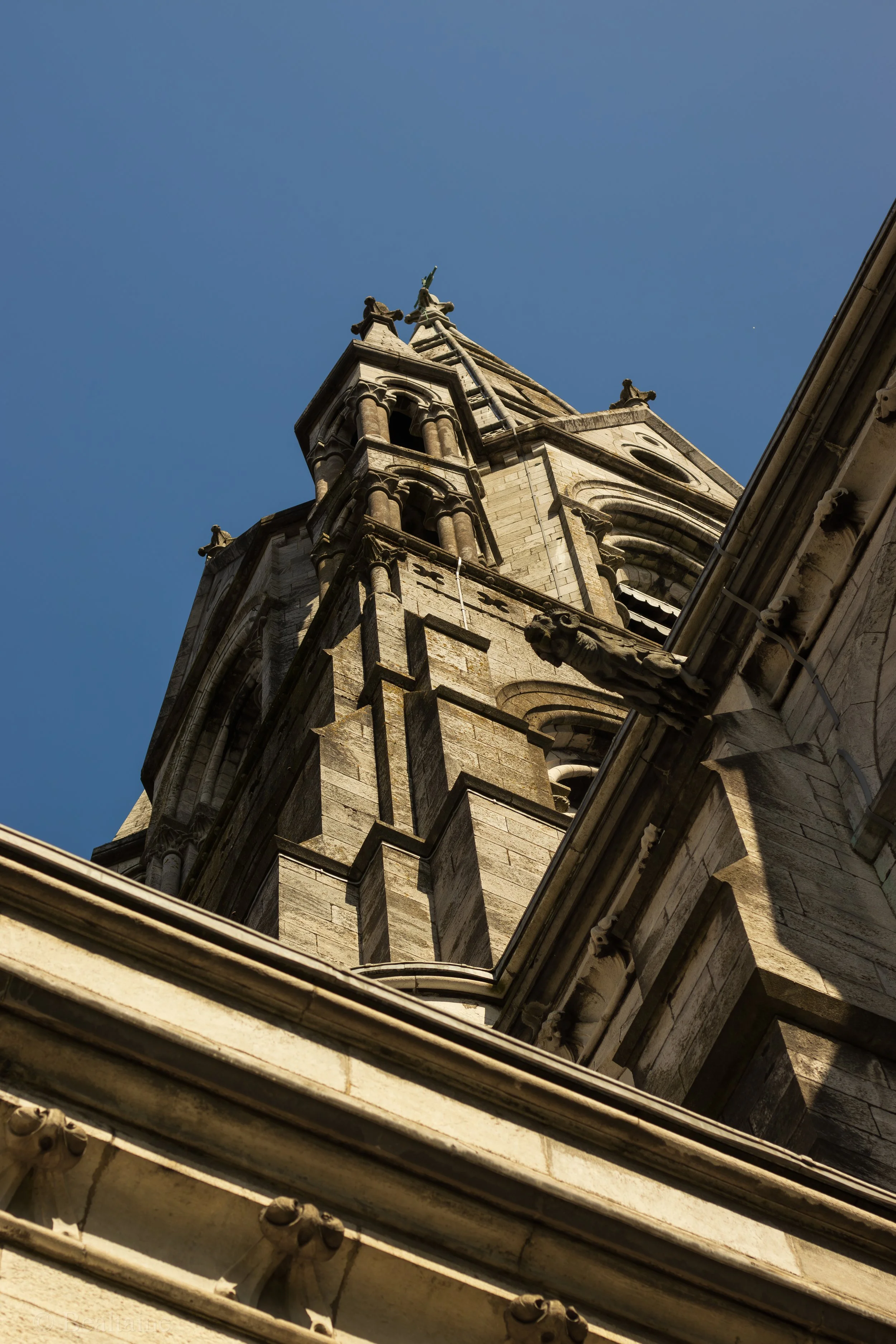 Low-angle view of a church steeple with ornate stonework against a blue sky.