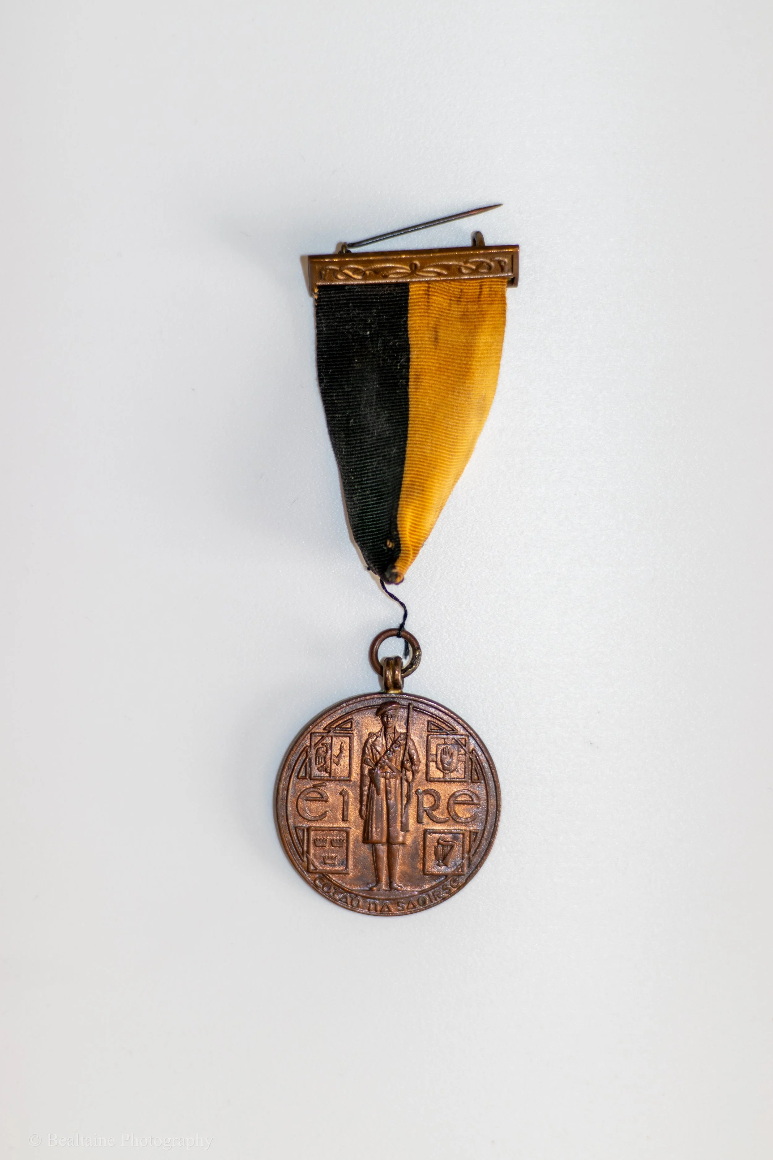 Close-up of a bronze military medal with a black and yellow ribbon. The medal features a figure of a soldier holding a rifle, with the words 'EIRE' and other inscriptions around the edge.