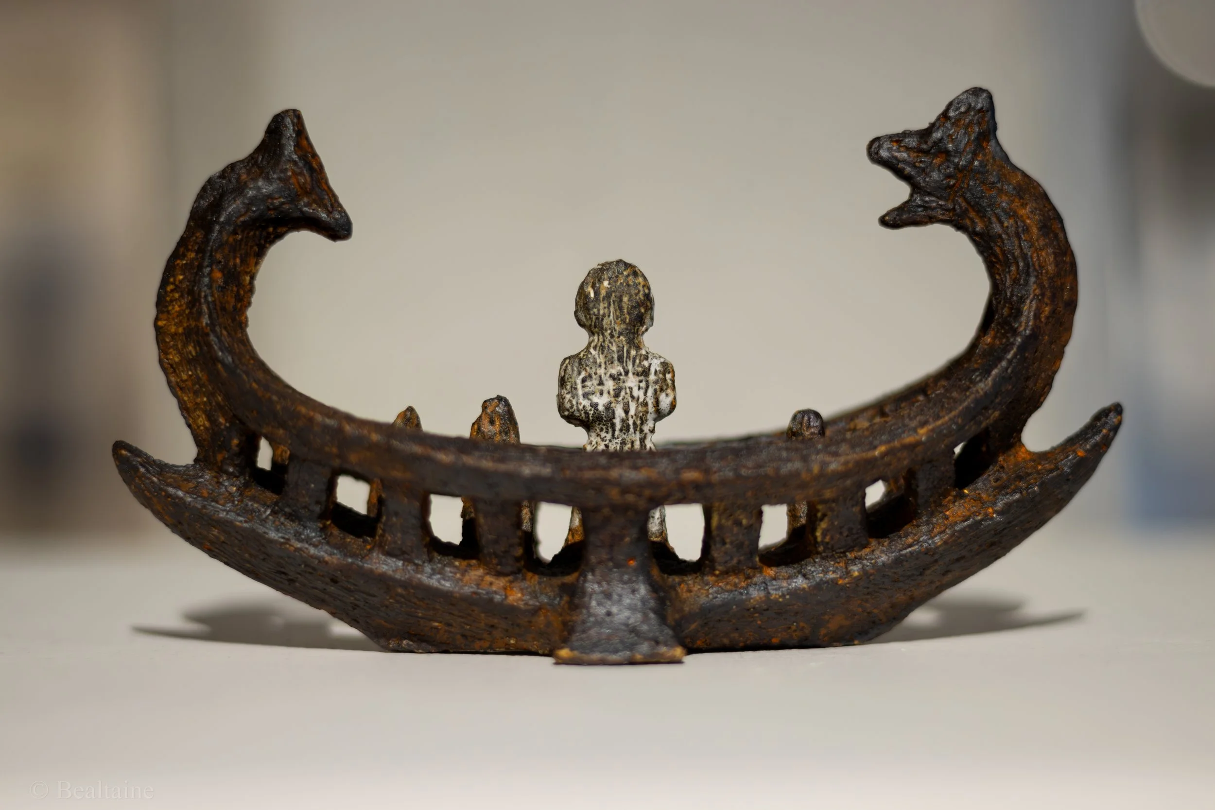 Close-up of a decorative metal crown with a small figure of a child or fragment in the center, showing a rustic, aged surface.