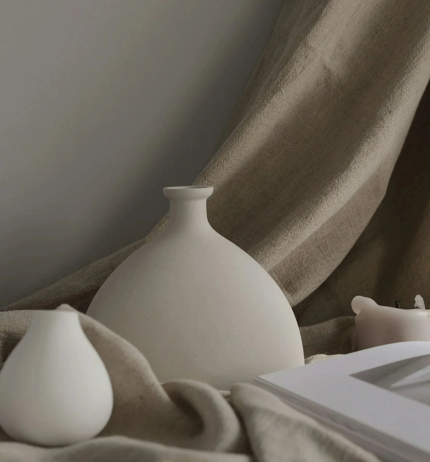 Close-up of white ceramic vases and a teapot on beige fabric with soft lighting.