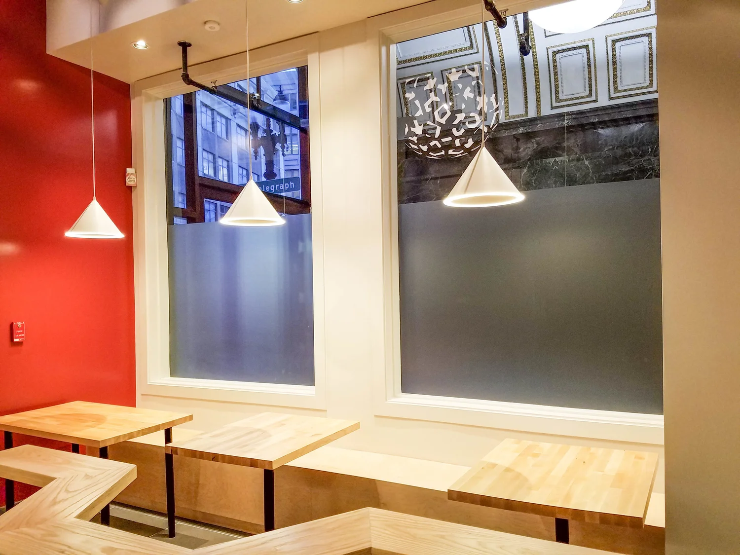 White pendant lights illuminate tables and custom wooden bench seating at the base of frosted windows.