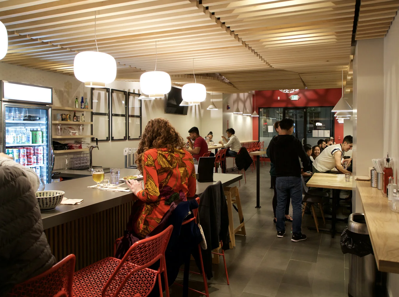 Customers dine and socialize in a mixture of bar and table seating, with custom milled wooden ceiling panels and countertops.